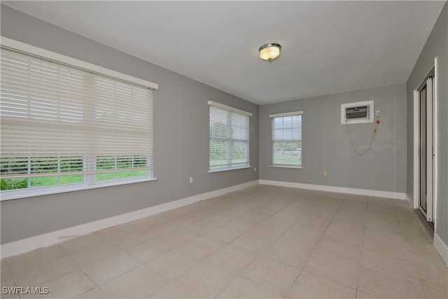 spare room featuring baseboards, light tile patterned floors, and a wall mounted air conditioner
