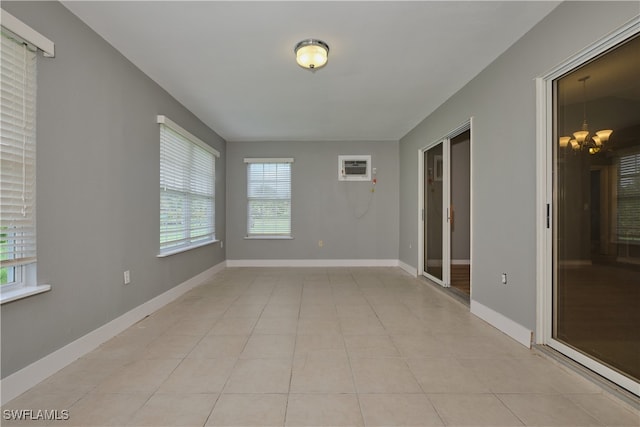 tiled spare room featuring an AC wall unit and an inviting chandelier