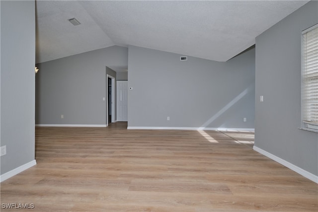 unfurnished living room featuring a textured ceiling, a wealth of natural light, light hardwood / wood-style flooring, and vaulted ceiling