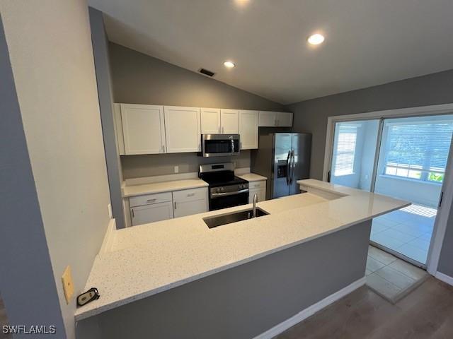 kitchen with a sink, a peninsula, white cabinets, lofted ceiling, and appliances with stainless steel finishes