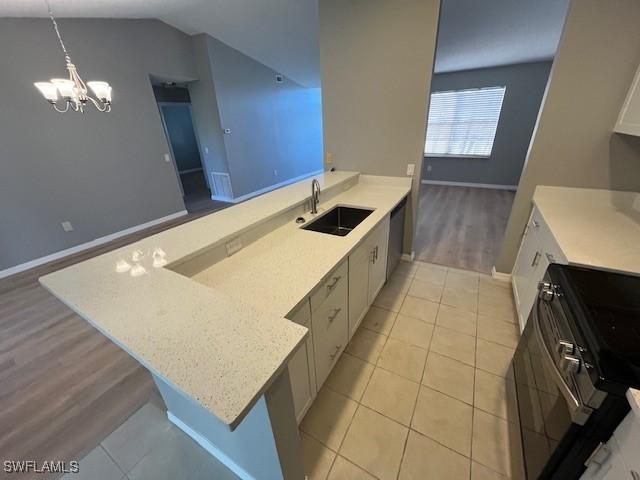 kitchen featuring an inviting chandelier, light tile patterned floors, a sink, a peninsula, and black range with electric cooktop