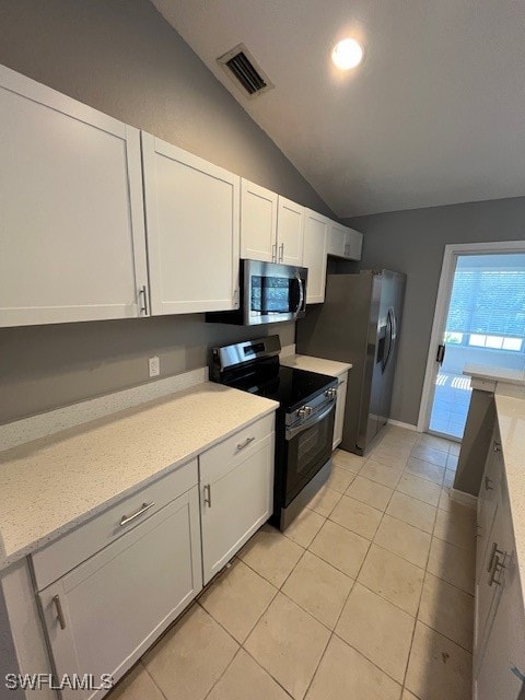 kitchen with lofted ceiling, white cabinets, appliances with stainless steel finishes, light tile patterned flooring, and light stone counters