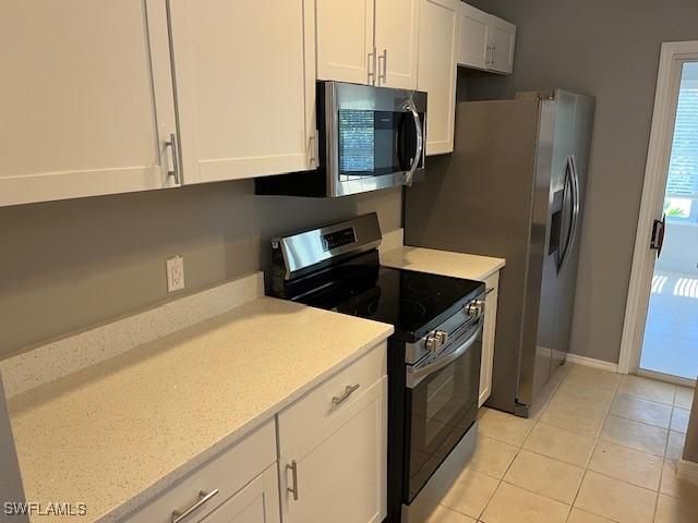 kitchen with baseboards, white cabinetry, appliances with stainless steel finishes, and light tile patterned flooring
