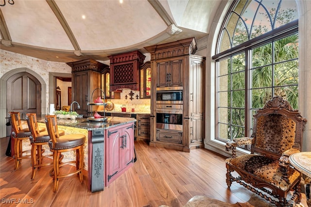 kitchen with a breakfast bar, light wood-type flooring, lofted ceiling, stainless steel double oven, and stone counters