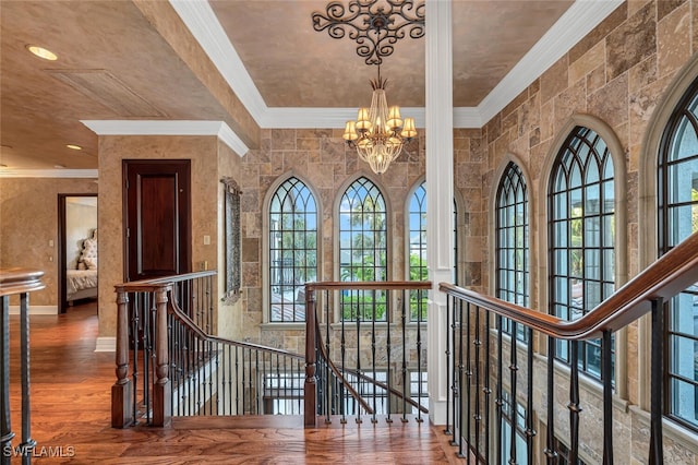 hallway featuring wood-type flooring, an inviting chandelier, ornamental molding, and a healthy amount of sunlight