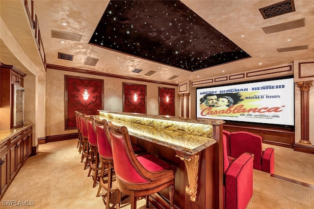 cinema with light carpet, a tray ceiling, and ornate columns