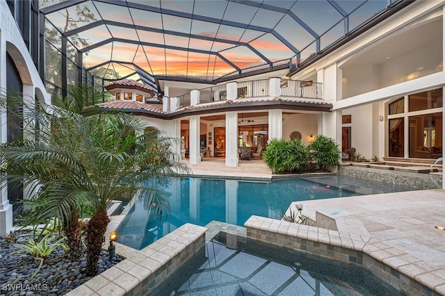 pool at dusk with glass enclosure, an in ground hot tub, and a patio