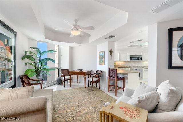 living room with ceiling fan and a raised ceiling