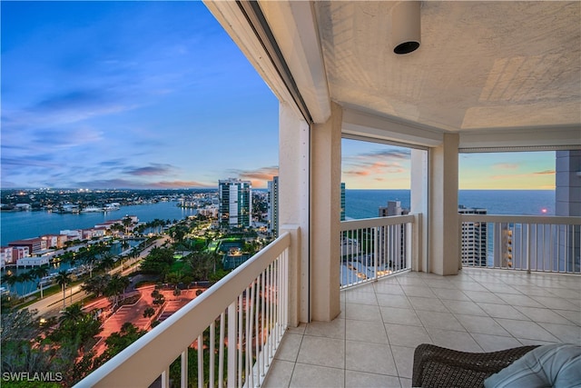 balcony at dusk featuring a water view