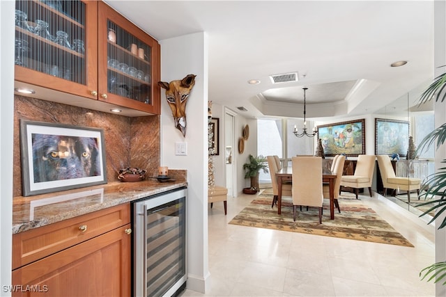 interior space featuring hanging light fixtures, wine cooler, light stone countertops, a raised ceiling, and tasteful backsplash