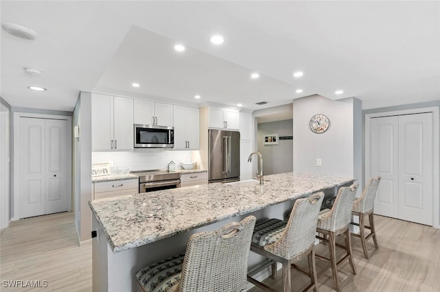 kitchen with light hardwood / wood-style floors, a large island with sink, stainless steel appliances, and white cabinets