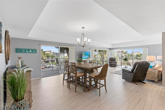 dining space with a notable chandelier, light hardwood / wood-style flooring, plenty of natural light, and a tray ceiling