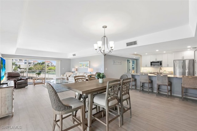 dining space with light wood-type flooring, a chandelier, and a tray ceiling