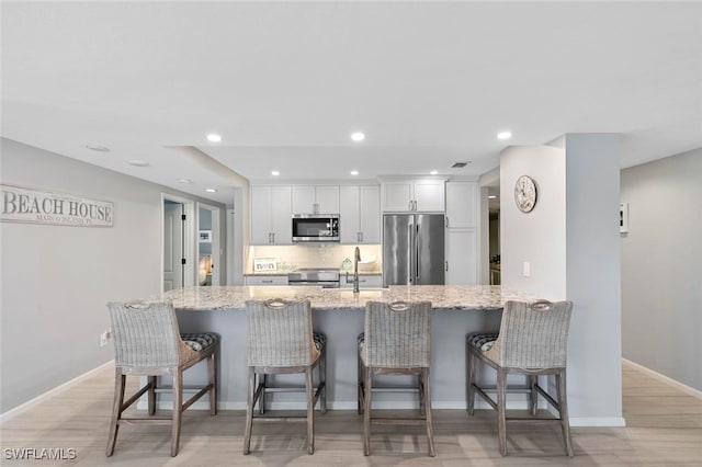 kitchen with light hardwood / wood-style floors, white cabinets, light stone countertops, stainless steel appliances, and a kitchen bar