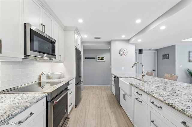 kitchen featuring light stone counters, sink, white cabinetry, appliances with stainless steel finishes, and light wood-type flooring