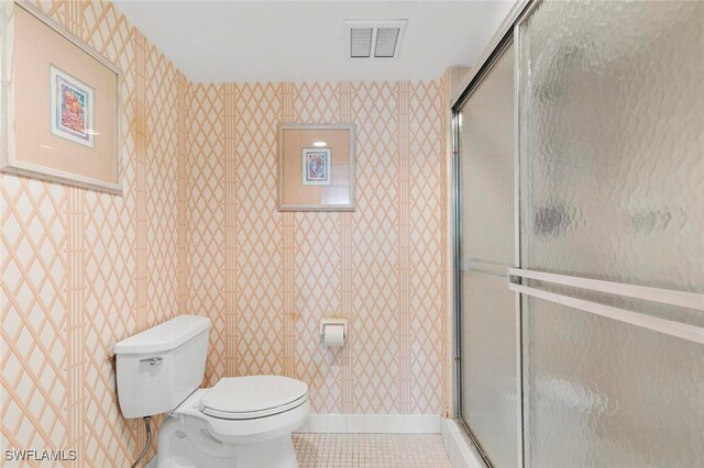 bathroom with tile patterned flooring, a shower with door, and toilet