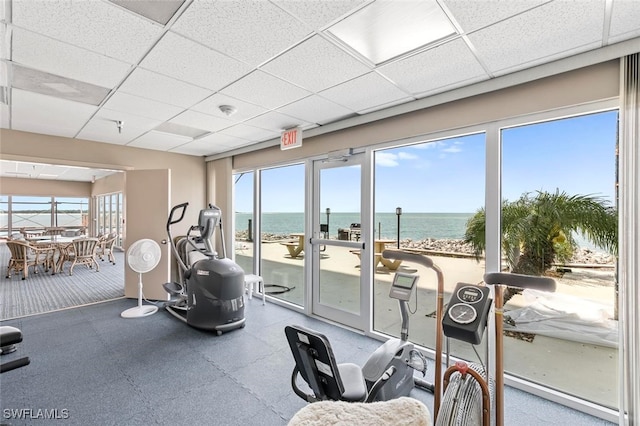 gym with a view of the beach, a water view, and a drop ceiling