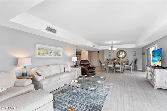 living room featuring a notable chandelier, light hardwood / wood-style floors, and a raised ceiling