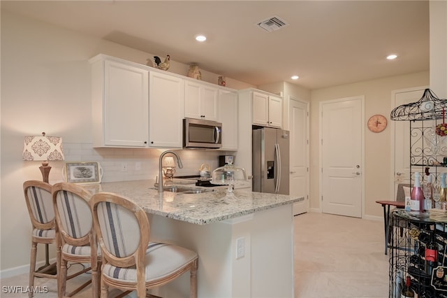 kitchen with appliances with stainless steel finishes, white cabinetry, tasteful backsplash, kitchen peninsula, and light stone countertops