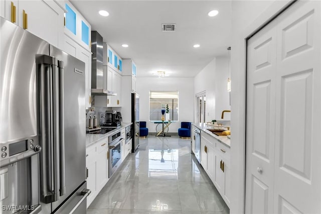 kitchen featuring white cabinets, decorative light fixtures, wall chimney range hood, stainless steel appliances, and sink