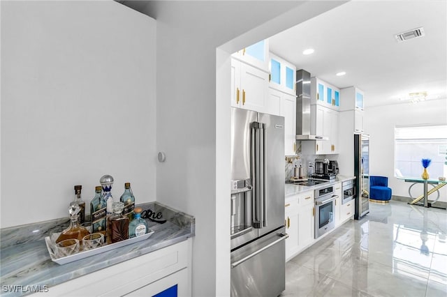 kitchen with wall chimney range hood, light stone counters, stainless steel appliances, and white cabinetry