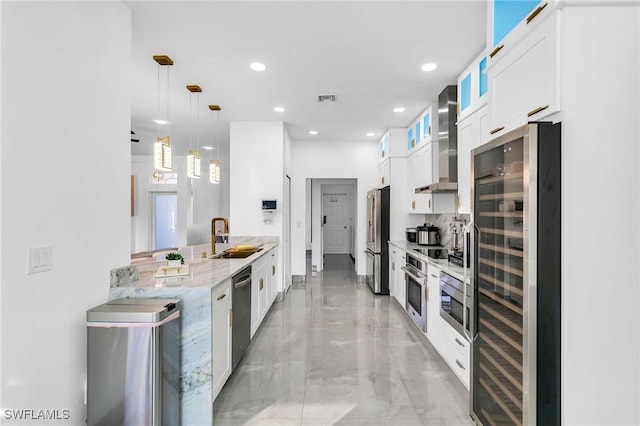 kitchen with sink, hanging light fixtures, appliances with stainless steel finishes, white cabinets, and wall chimney exhaust hood