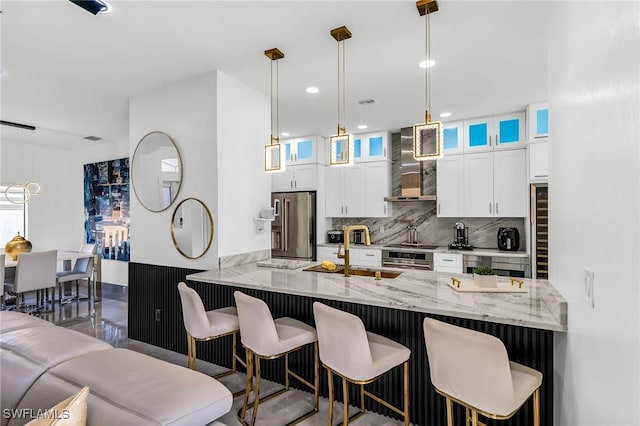 kitchen with kitchen peninsula, a breakfast bar area, stainless steel appliances, wall chimney range hood, and light stone counters