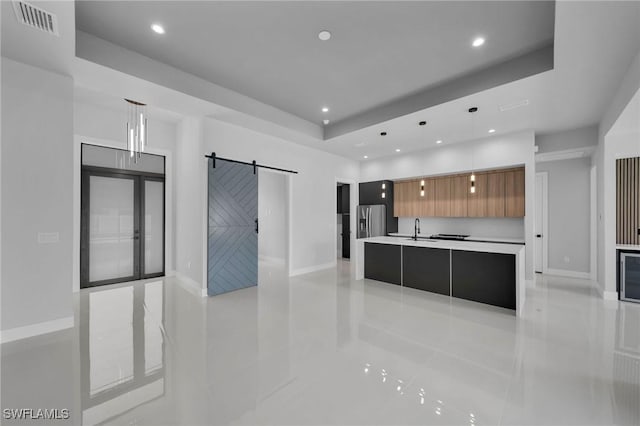 kitchen featuring pendant lighting, an island with sink, a raised ceiling, a barn door, and sink