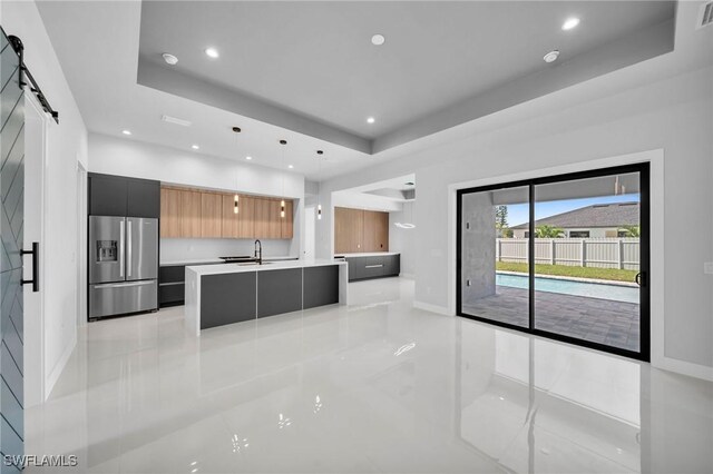 kitchen with decorative light fixtures, a barn door, stainless steel fridge, a center island with sink, and a tray ceiling