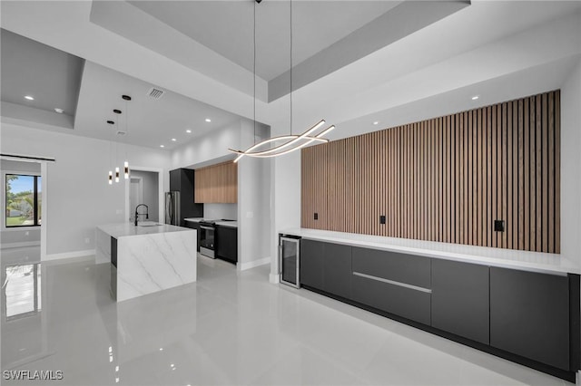 kitchen featuring electric range oven, an island with sink, modern cabinets, a tray ceiling, and a sink