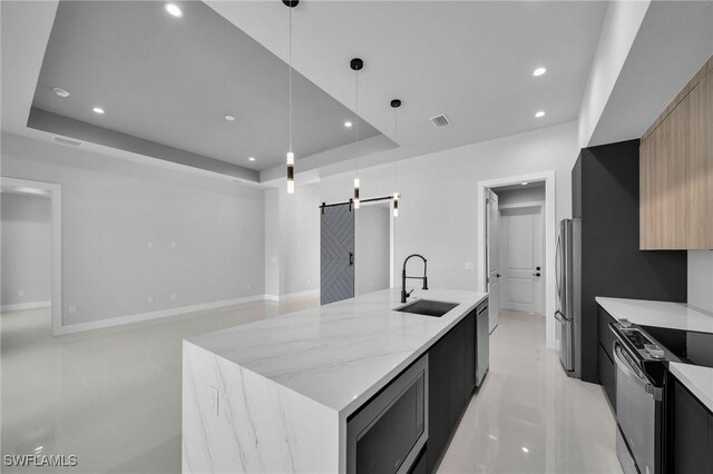 kitchen with sink, hanging light fixtures, a barn door, a kitchen island with sink, and appliances with stainless steel finishes