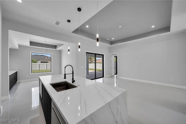 kitchen featuring sink, decorative light fixtures, light stone countertops, a center island with sink, and a tray ceiling