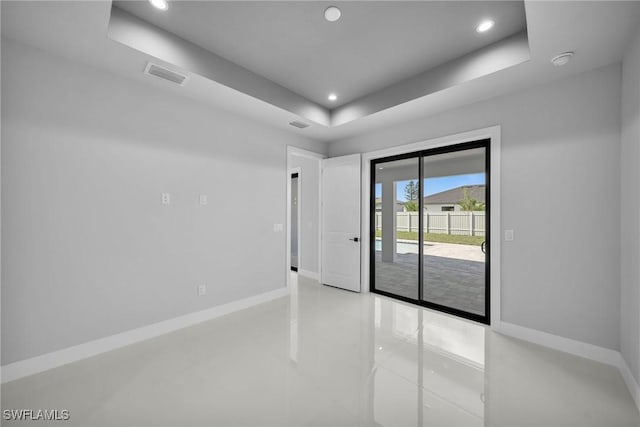 empty room with a tray ceiling, recessed lighting, visible vents, and baseboards