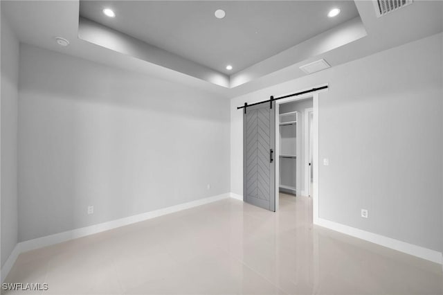 unfurnished bedroom with a raised ceiling, visible vents, baseboards, and a barn door