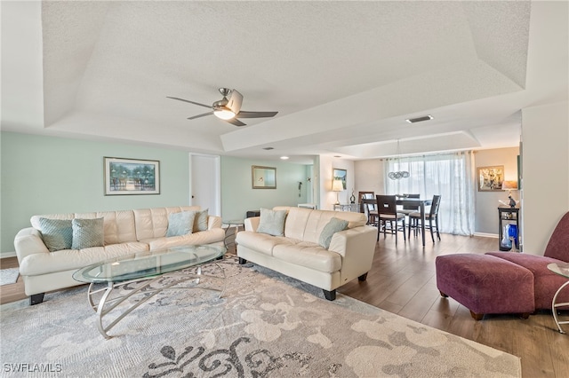 living room with ceiling fan, a textured ceiling, light hardwood / wood-style flooring, and a raised ceiling