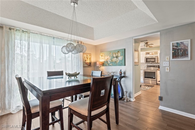 dining area with ceiling fan, hardwood / wood-style flooring, a tray ceiling, and a textured ceiling