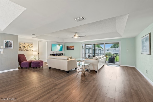 living room with ceiling fan, a textured ceiling, and dark wood-type flooring