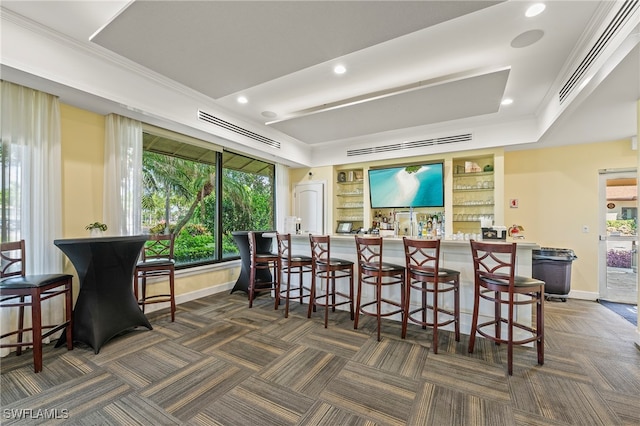 bar featuring ornamental molding, dark colored carpet, and a raised ceiling