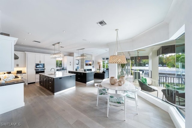 kitchen with an island with sink, built in microwave, light countertops, white cabinetry, and pendant lighting