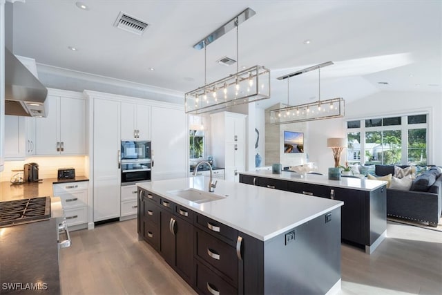 kitchen with a sink, visible vents, white cabinetry, a center island with sink, and pendant lighting