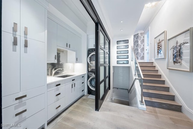 interior space featuring white cabinets, stacked washer and clothes dryer, modern cabinets, light countertops, and a sink