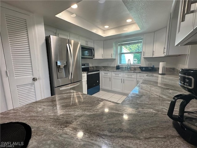 kitchen with white cabinetry, dark stone countertops, appliances with stainless steel finishes, and a tray ceiling