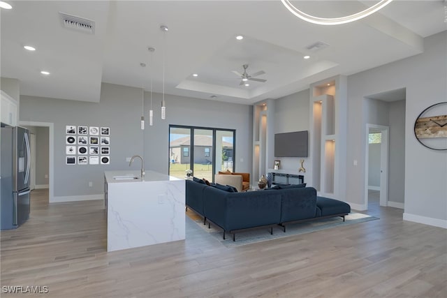 living room with a raised ceiling, ceiling fan, sink, and light hardwood / wood-style floors