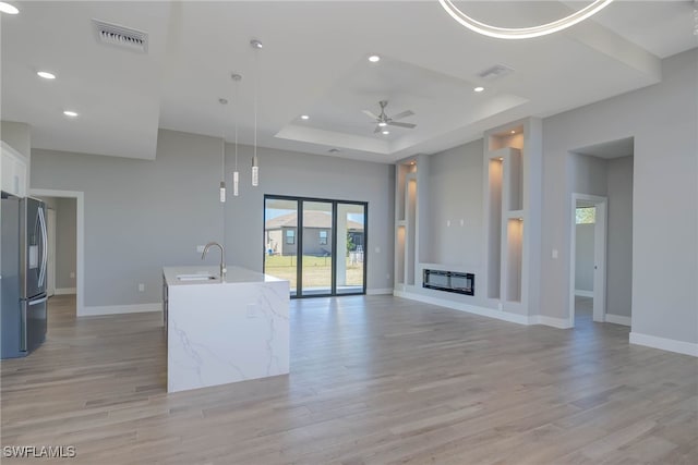 unfurnished living room with light wood-type flooring, a raised ceiling, ceiling fan, and sink