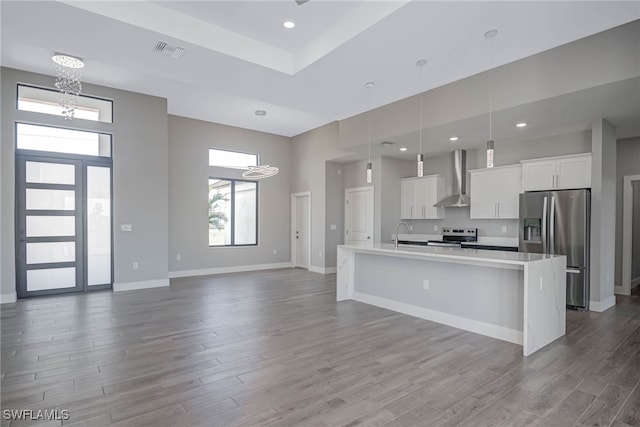 kitchen with white cabinetry, hanging light fixtures, stainless steel appliances, wall chimney range hood, and a large island with sink