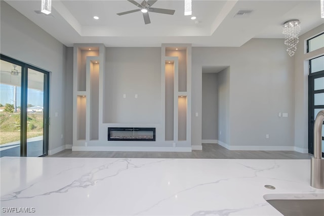 unfurnished living room featuring ceiling fan and a raised ceiling