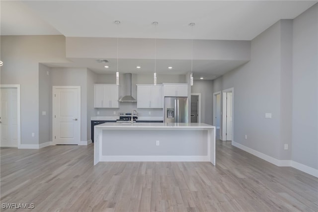 kitchen with white cabinetry, wall chimney exhaust hood, an island with sink, decorative light fixtures, and appliances with stainless steel finishes