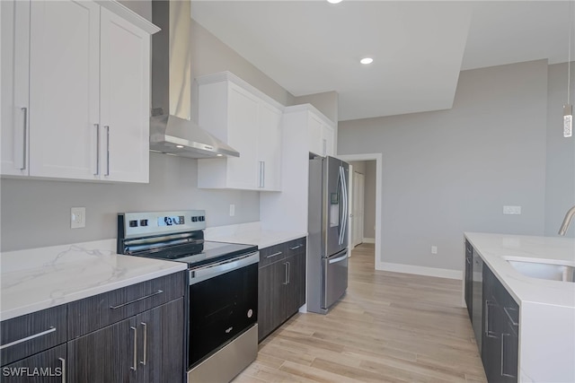 kitchen with white cabinetry, sink, wall chimney range hood, light hardwood / wood-style flooring, and appliances with stainless steel finishes