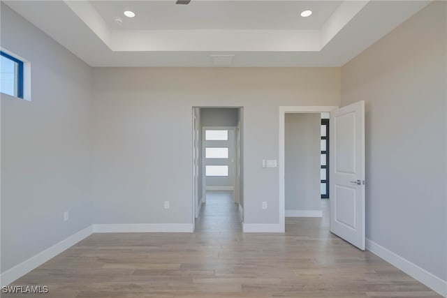 unfurnished room with a tray ceiling and light wood-type flooring