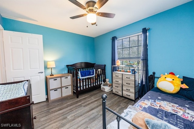 bedroom featuring hardwood / wood-style floors, a nursery area, and ceiling fan